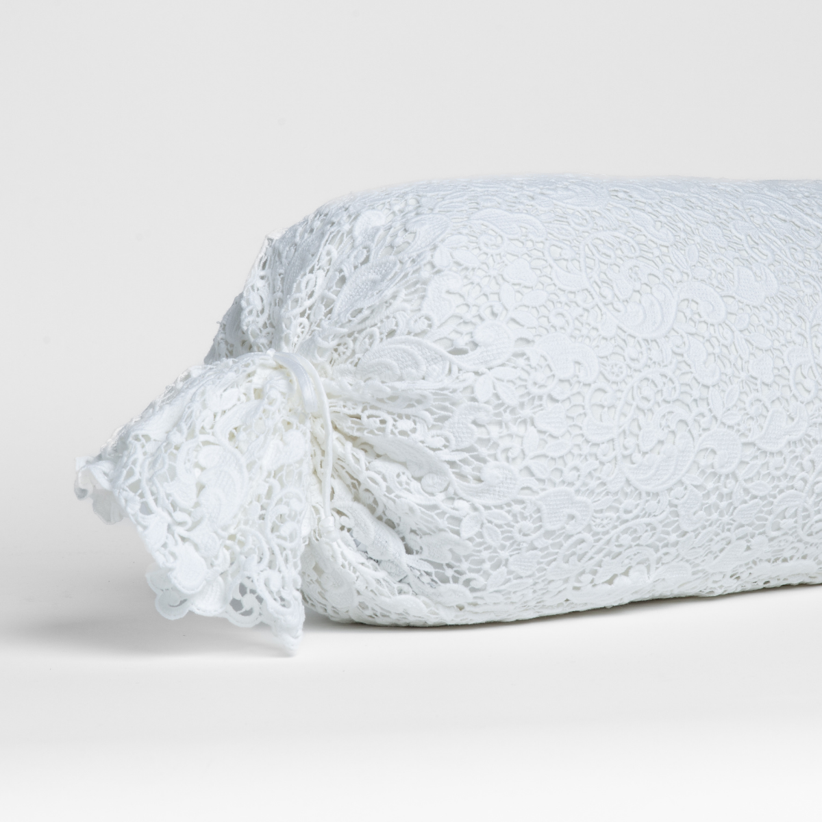 White:  one end of a lace boslter cover on a winter white liner against a white background.
