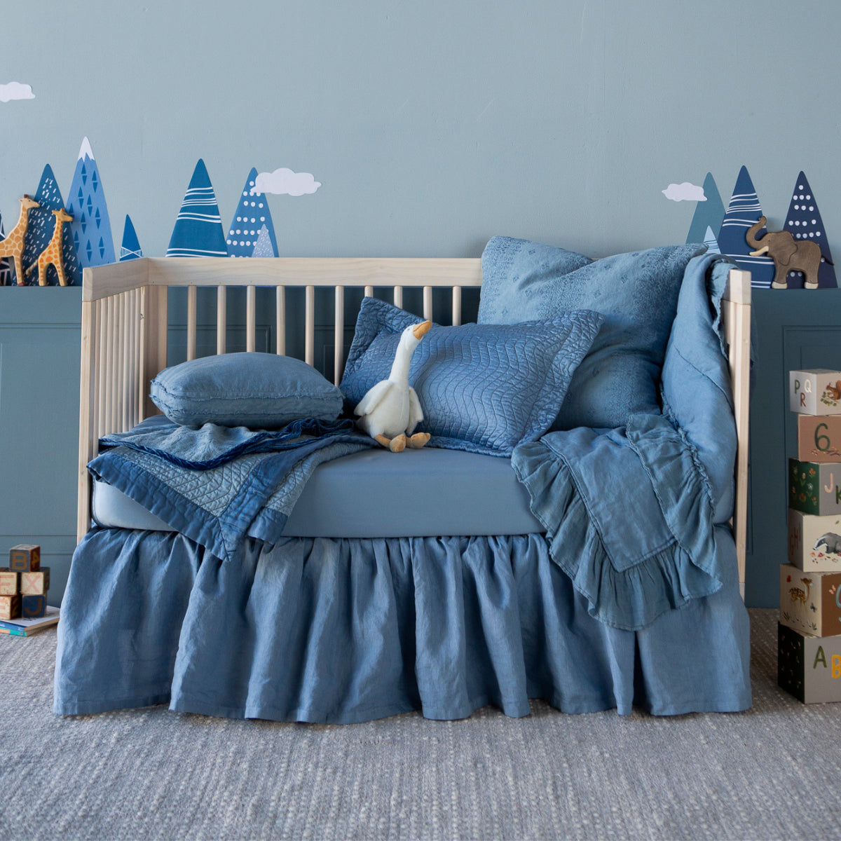 An all-blue crib styled as a toddler bed with toys scattered about the scene and tree decals on the wall.