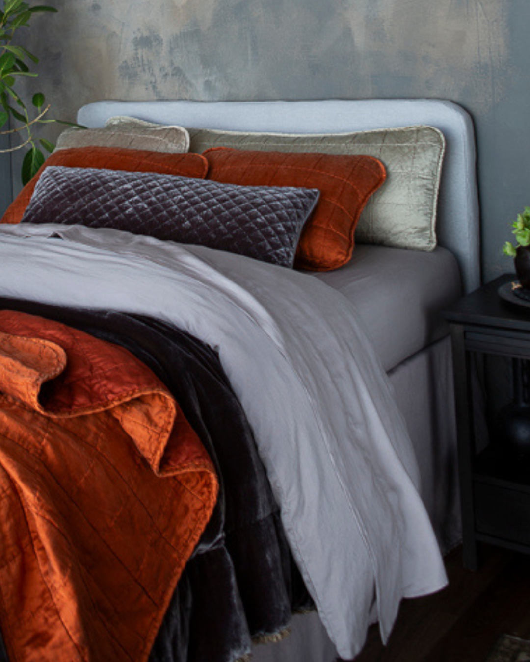 A top half of bed dressed with Sel Throw Pillows in Moonlight (18x54 & 18x18) and Silk Velvet Quilted Throw Pillow (16x36) in Moonlight with Sel Shams in Autumn on a bed layered with Madera Luxe Sheets and Duvet Cover in Moonlight. Carmen Blanket at the bed end and Sel Throw Blanket in Autumn, finished with the Austin Bed Skirt in Moonlight.