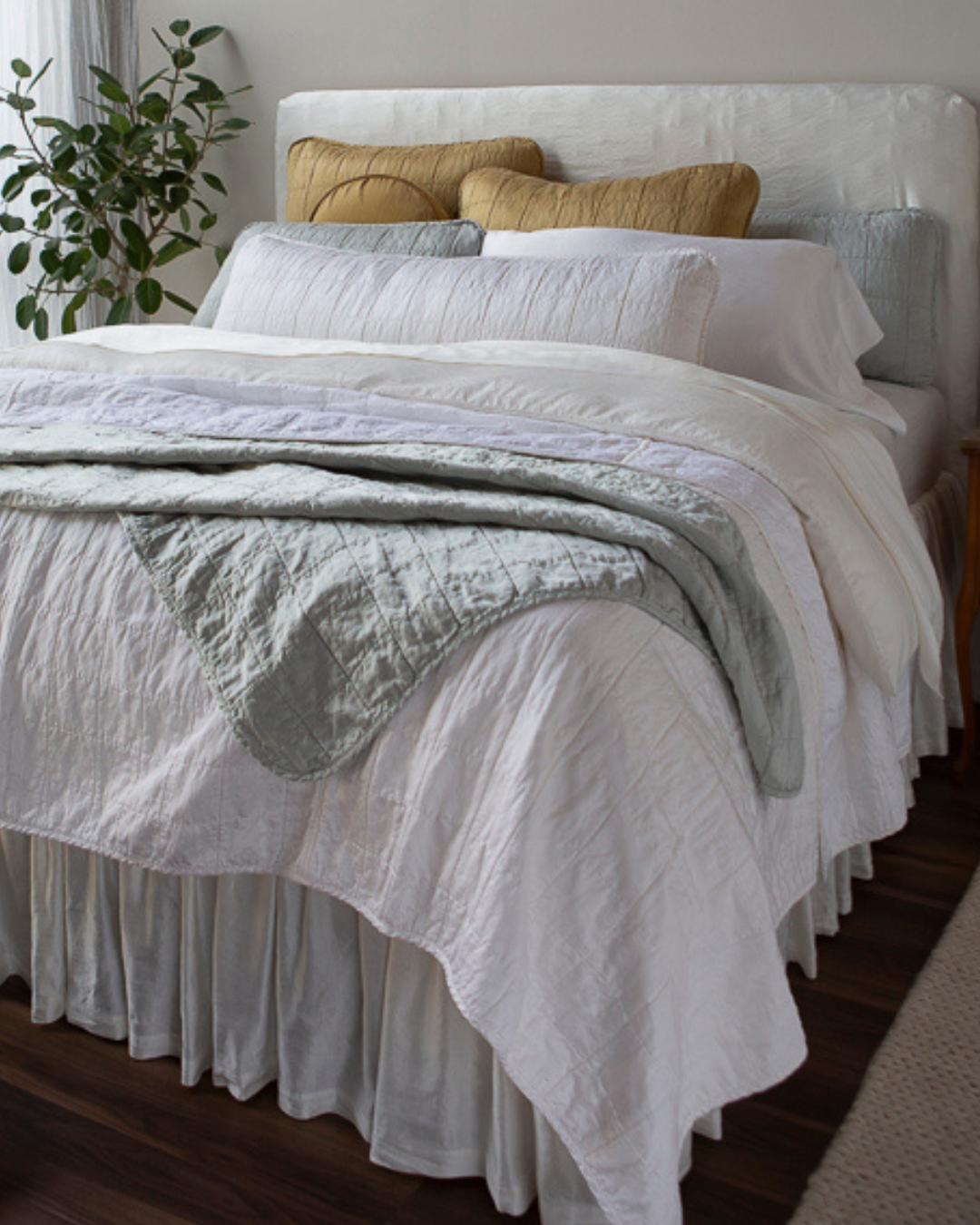 A corner shot of a bed dressed mostly in shades of White with hints of Cloud and Honeycomb. This bed celebrates the addition of Sel to our lineup
of fabric collections. Continue the honeymoon once you’re back
home with this look.