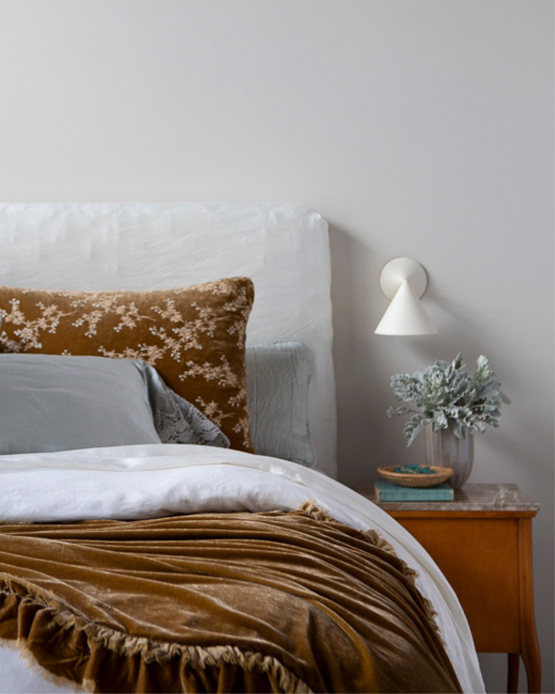 A bed shot featuring our Lynette Luxe collection is front and center here in a honeycomb hue against a light-colored bedding ensemble. A wooden night stand with decor on stop sits next to the bed.