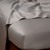Bria Twin Flat Sheet | Fog | Cotton sateen flat sheet draped over matching fitted sheet. Shown from the top corner, the flat sheet is rumpled, highlighting the shine of the fabric.