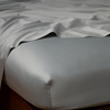 Bria Twin Flat Sheet | Mineral | Cotton sateen flat sheet draped over matching fitted sheet. Shown from the top corner, the flat sheet is rumpled, highlighting the shine of the fabric.