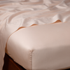 Bria Twin Flat Sheet | Pearl | Cotton sateen flat sheet draped over matching fitted sheet. Shown from the top corner, the flat sheet is rumpled, highlighting the shine of the fabric.