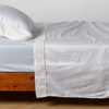 Bria Flat Sheet | White | Cotton sateen sleeping pillow and flat sheet embellished with cotton lace trim on a bed - side view.
