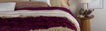 a close up of a bed dressed in several layers and multiple colors with the lace at the foot of the bed  most in focus. 