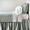 Eucalyptus | The Adele coverlet in eucalyptus, on a bed viewed from the side against a plain white wall. The bed is styled neatly with the coverlet folded back to reveal white sheets, bed skirt and pillows.