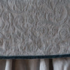 Mineral | Close up of the Adele coverlet in mineral, highlighting the detail of the cotton damask and the silk velvet edging trim. A white bed skirt peeks out at the bottom of the shot.