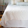 Austin bed skirt in winter white, shown from the end of the bed, layered with a quilted coverlet in the same tone.