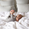 White | Playful baby laying on rumpled Austin duvet cover with shams and pillows in the background.