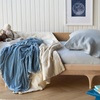 Linen Crib Sheet | Crib sheet in cloud shown on a wooden toddler bed with cream and blue rumpled blankets.