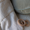 Ines Baby Blanket | Close up of rumpled blanket in winter white highlights embroidery, shown with a pale green pillow and wooden teether toys.