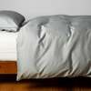 Bria Twin Duvet Cover | Cotton sateen duvet cover in mineral with matching sleeping pillow on white sheeting - side view.