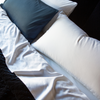Bria flat sheet in white, shown folded over a coverlet from an overhead angle, with side by side sleeping pillows in white and midnight blue.