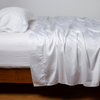 Bria Flat Sheet | White | Cotton sateen flat sheet, shown with matching fitted sheet and sleeping pillow - side view.