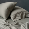 Bria Pillowcase (Single) | Eucalyptus | Bria sleeping pillows in eucalyptus angled asymmetrically against a moody dark background. Matching sheets are ruimpled in the foreground.