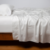 Bria Pillowcase (Single) | Winter White | Cotton sateen sleeping pillow, on a bed with matching sheets - side view.