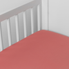 Bria Crib Sheet | Poppy | Cotton sateen crib sheet shown from a slight overhead angle into  an inside corner of a crib.