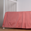 Bria Crib Skirt | Poppy | cotton sateen cribi skirt with a center pleat shown straight on from a slight angle in a crib without a crib mattress.