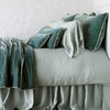 Carmen Blanket | Eucalyptus | Silk velvet throw blanket with petite ruffle, draped across a monochromatic bed - side view.