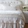 Carmen shams in winter white on a monochromatic bed, stacked behind sleeping and throw pillows - view from end of bed.