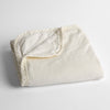 Harlow Baby Blanket | Winter White | cotton velvet baby blanket trimmed with charmeuse, folded with a covern folded back to show trim contrast; shot overhead and at a slight angle against a white background.