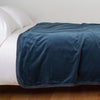 Harlow Blanket | Midnight | Cotton velvet bed end sized blanket, draped on a white bed - side view.