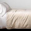 Harlow Blanket | Parchment | Cotton velvet bed end sized blanket, draped on a white bed - side view.