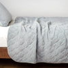 Harlow Coverlet | Cloud | Quilted cotton velvet coverlet draped over a white fitted sheet - side view.
