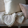 Harlow Blanket | Close-up of Harlow throw blanket in parchment folded under light neutral throw pillows, showcasing shining carmeuse trim.