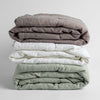 Ines Baby Blanket | A stack of three embroidered linen baby blankets in  moonlidhgt, white and eucalyptus.