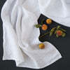 White Ines guest towel draped on a dark background scattered with baby apricots and green leaves - overhead view.