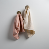 Two Ines guest towels, draped over decorative hooks against a white wall - rouge and parchment.