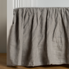 Linen Crib Skirt | Mineral | crib skirt shown on a white crib with no mattress against a white wall and medium wood flooring.