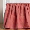 Linen Crib Skirt | Poppy | crib skirt shown on a white crib with no mattress against a white wall and medium wood flooring.