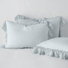 Linen Whisper Sham | Cloud | two shams leaning upright and one laying flat at an angle in the foreground, against a blank background.