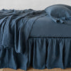 Linen Twin Bed Skirt | Linen bed skirt in midnight, with matching rumpled sheets and sleeping pillows - side view.