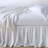 Linen Twin Bed Skirt | White | bed skirt with matching rumpled sheets and sleeping pillows - side view.