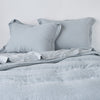 Linen Twin Duvet Cover | Mineral | duvet cover partially folded back on a bed with matching sheets and shams against a white wall - cropped end of bed view.