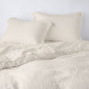 Linen Twin Duvet Cover | Parchment | duvet cover partially folded back on a bed with matching sheets and shams against a white wall - cropped end of bed view.