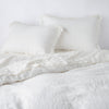 Linen Twin Duvet Cover | Winter White | duvet cover partially folded back on a bed with matching sheets and shams against a white wall - cropped end of bed view.