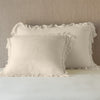 Loulah Sham | Parchment | shams leaning upright on white sheets against a neutral headboard.