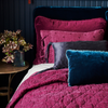Luna coverlet on a fig bed, with mixed textures of cotton velvet, embroidered linen, tassled silk charmeuse, and silk velvet. Deep blue throw pillows and dark blue background create a moody vibe.