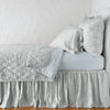 Luna Coverlet | Cloud | coverlet neatly folded back to reveal linen reverse, on a monochromatic bed - side view.