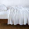 Madera Luxe Twin Flat Sheet | White | Rumpled flat sheet with matching fitted sheet and sleeping pillow - side view.