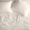Madera Luxe Pillowcase (Single) | Parchment | sleeping pillows laid flat over rumpled matching sheeting - overhead view.