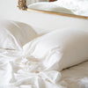 Madera Luxe Pillowcase (Single) | Madera Luxe sleeping pillows and sheeting in winter white, rumpled against a white wall with an antique gold frame mirror partially visible.