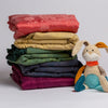 Mirabella Baby Blanket — Limited Release | a stack of bold rainbow colored silk and tencel™ baby blankets shown with a colorful stuffed bunny.