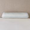 Paloma Throw Pillow | Cloud | bolster on white sheets with a neutral headboard.