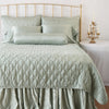 Paloma Throw Pillow | Eucalyptus | Paloma bolster on a monochromatic, all-charmeuse bed - eucalyptus, end of bed view.